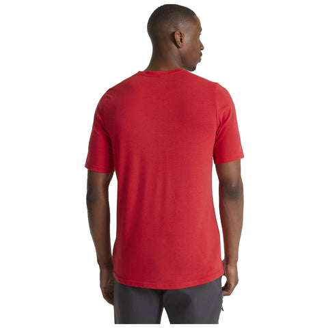 A person wearing a red short-sleeve shirt stands facing away, showing the back of the shirt in a neutral, well-lit setting without additional context or items around.