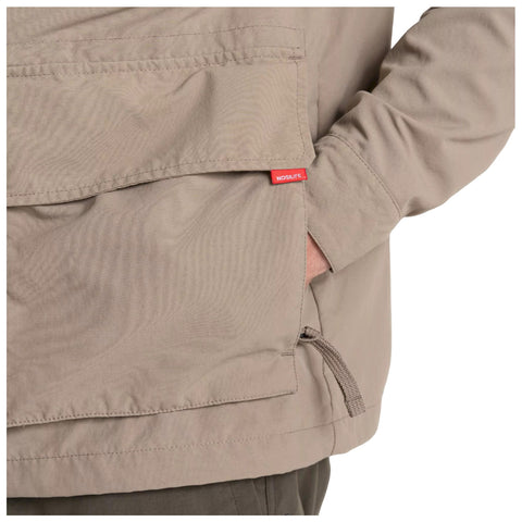 A person is wearing a beige jacket with a large front pocket and a logo tag visible on the pocket while casually placing a hand inside the pocket.