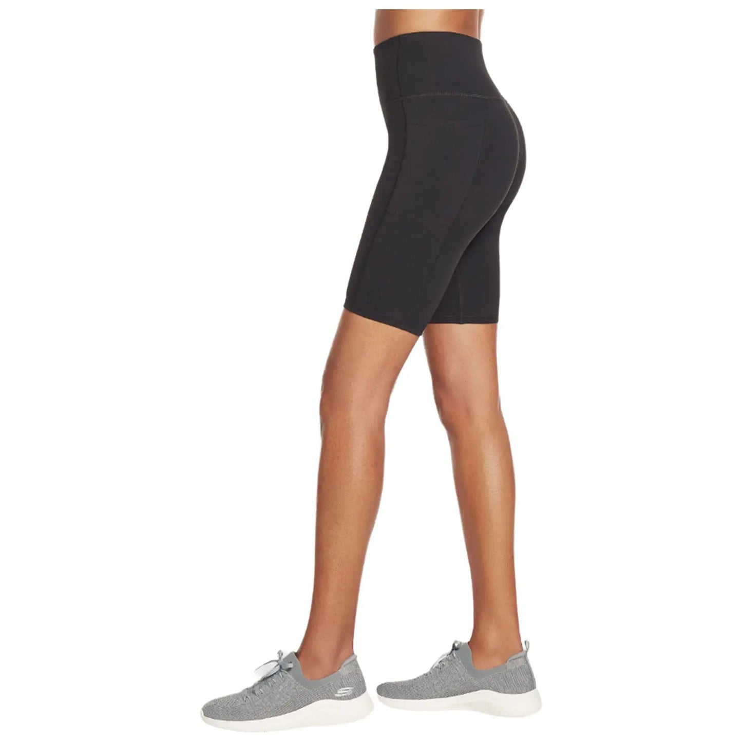 Black high-waisted shorts fit snugly to the hips and thighs while a person stands sideways wearing gray athletic shoes in a minimalistic setting.