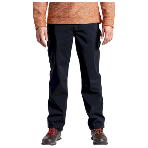 A person stands wearing black pants and brown boots with orange laces while wearing an orange long-sleeve shirt in a neutral background.