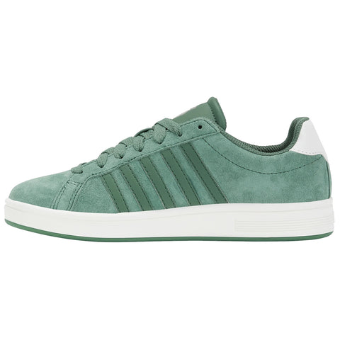A green suede sneaker sits upright displaying six lace holes and three vertical stripes on its side while featuring a white heel cap in a neutral background.