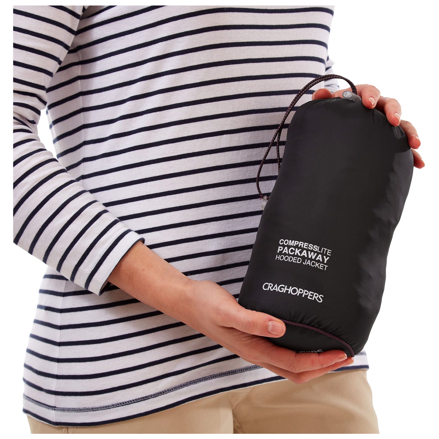 A person wearing a striped shirt holds a compressed black packaway jacket in one hand showcasing its compact size and portability while exuding a casual outdoor vibe. Text on the jacket reads "COMPRESSLITE PACKAWAY HOODED JACKET CRAGHOPPERS".