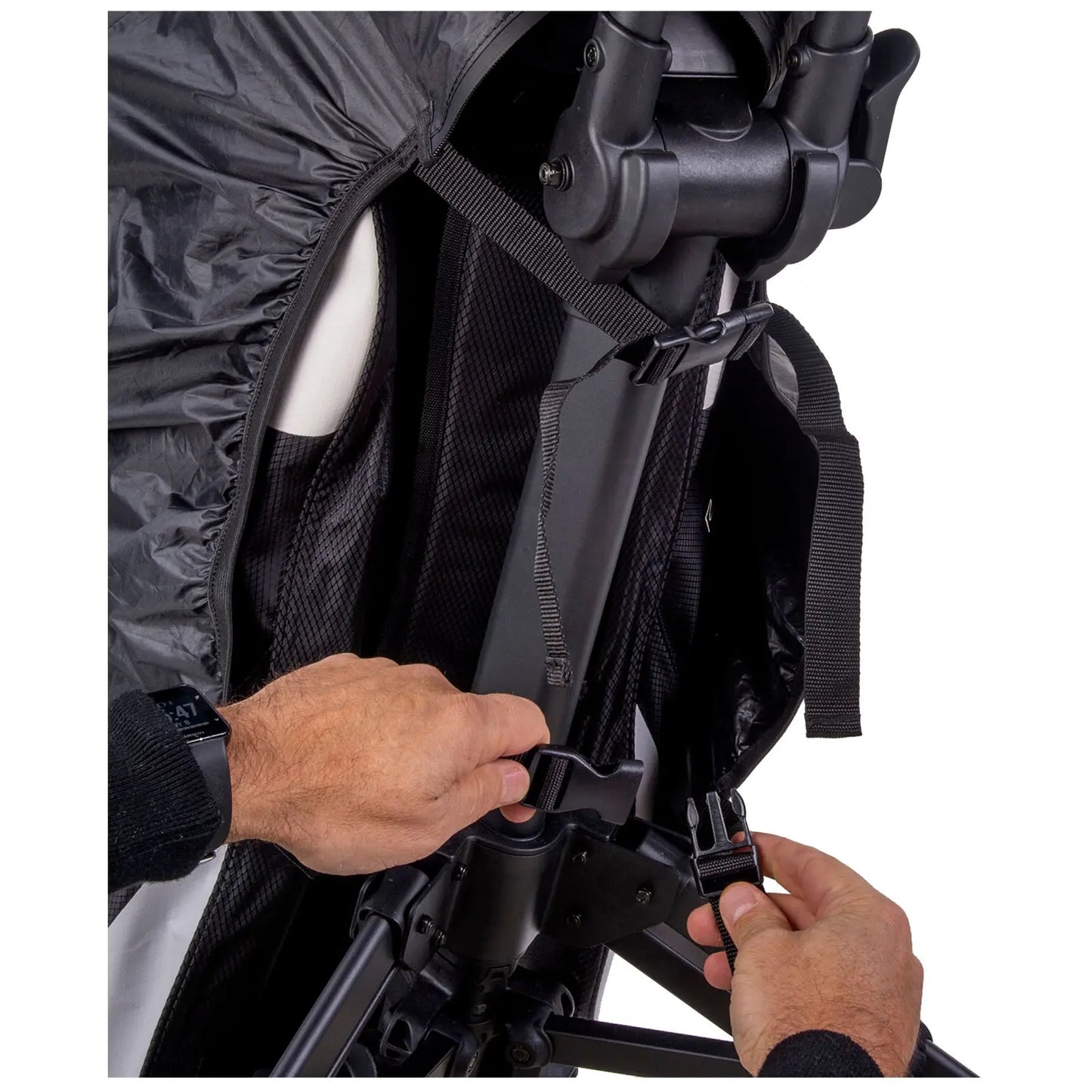 A person's hand adjusts a buckle on a black fabric cover attached to a chair's frame in a neutral setting with a focus on the mechanism and fabric details.