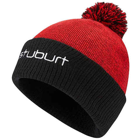 A red knitted beanie with a black band displays the word stuburt and features a fluffy pom-pom on top designed for warmth in cold weather environments.