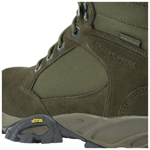 A rugged green boot features suede and textile materials with metal eyelets and a Vibram sole designed for traction and support in outdoor environments.