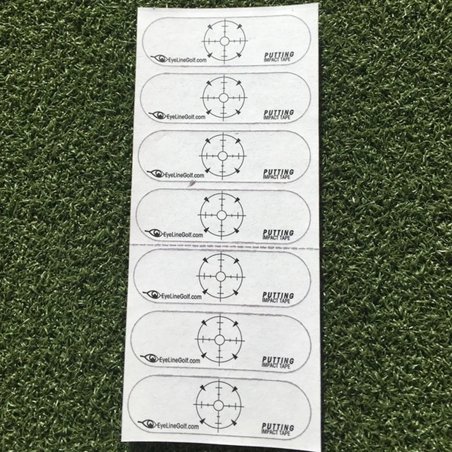 A series of adhesive strips with a target design is laid on artificial grass. Each strip is labeled "PUTTING IMPACT TAPE" and displays a circular crosshair pattern for golf practice.