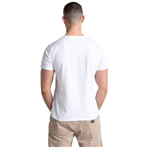 A man with short hair stands facing away wearing a plain white t-shirt and beige trousers in a neutral background creating a simple casual appearance