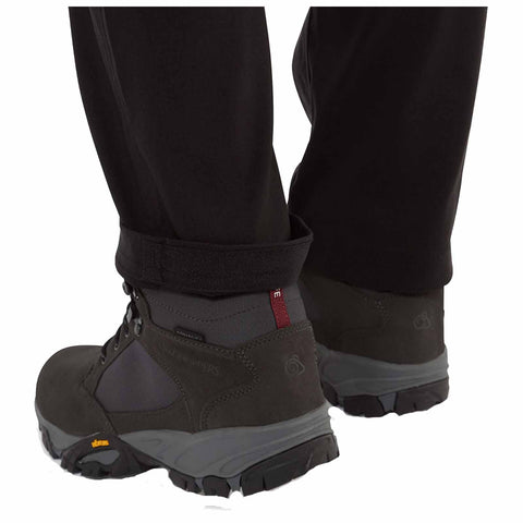 Hiking boots are positioned on a surface with the pant cuffs slightly rolled up revealing the boots designed for outdoor activities in a rugged environment.
