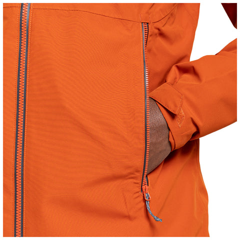 An orange jacket with a zippered pocket is partially unzipped and a hand is placed inside the pocket suggesting casual use in a neutral setting.