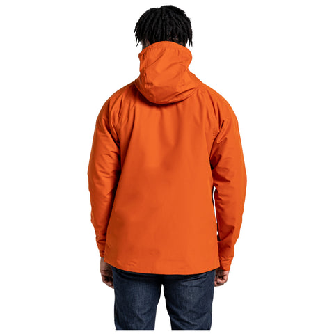 A person stands with their back facing the viewer wearing an orange hooded jacket and jeans in a plain white background. Their hair is styled in short, textured twists.