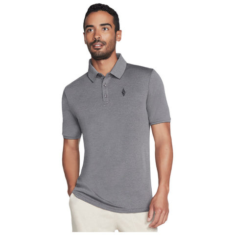 A man wearing a fitted gray polo shirt with a collar stands facing slightly right. He has a light beard, short hair, and is smiling, appearing confident in a neutral background.