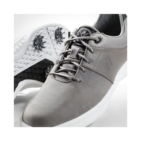 Gray golf shoes are positioned prominently with one shoe facing forward and the other angled slightly revealing detailed texture on the sole in a light-colored studio background.