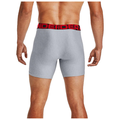A person is standing with their back to the viewer wearing gray boxer briefs with a red waistband displaying the word "UNDERARMOUR" in bold letters. The setting is neutral, focusing on the apparel.