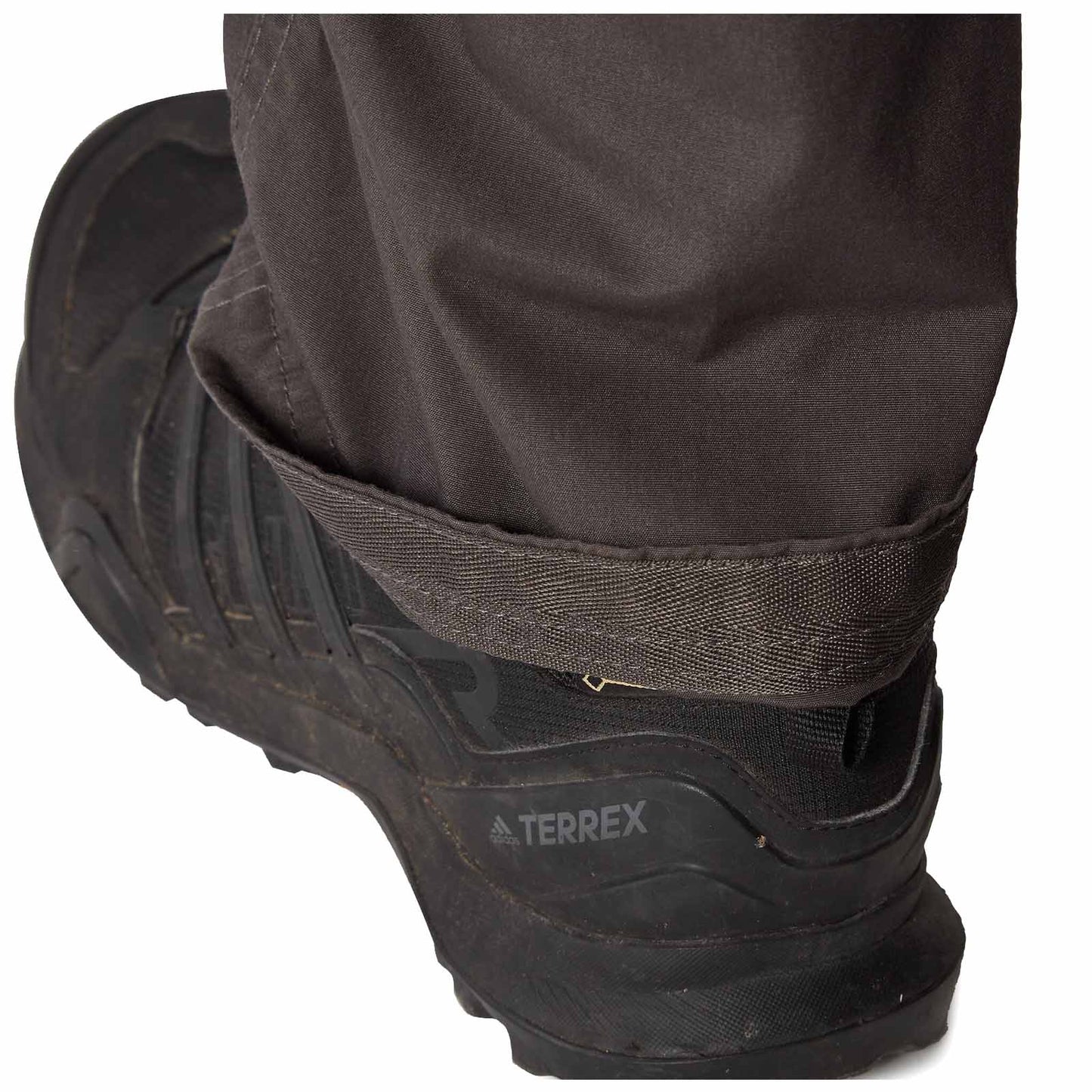 A black hiking shoe with the brand name Terrex is partially visible on a muddy surface while the cuff of a pair of brown pants rests over the shoe's edge.