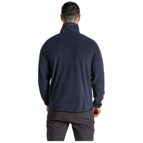 A man is standing with his back facing the viewer wearing a dark blue fleece jacket and dark pants in a neutral background suggesting an indoor setting.
