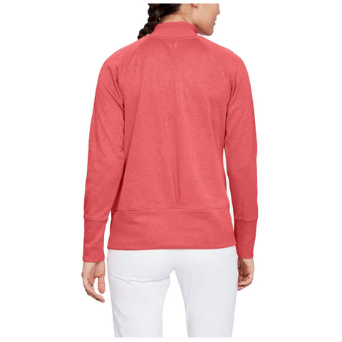 A woman stands facing away, wearing a pink sweatshirt with a high collar and fitted sleeves, positioned in a neutral space that highlights the garment's color and design.