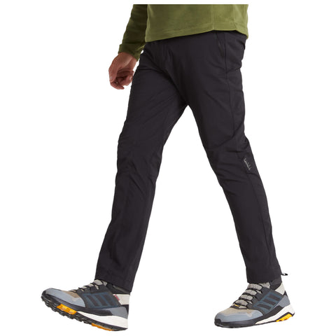 A person walks forward wearing black pants and gray hiking shoes with yellow soles in a casual outdoor setting, suggesting an active lifestyle or a light hiking activity.