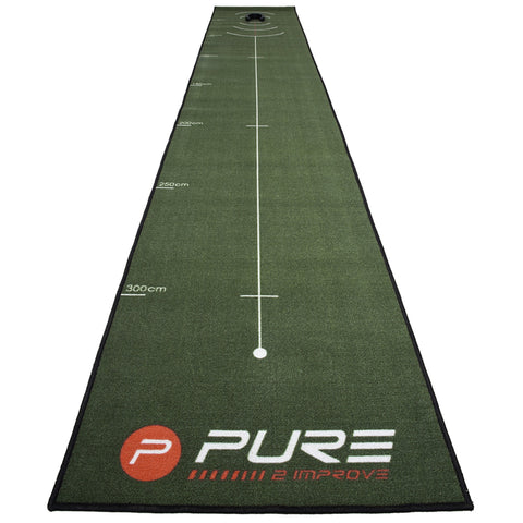 A long green putting mat with a white target hole at one end displays measurement markings in centimeters along the sides designed for practicing golf putting indoors.