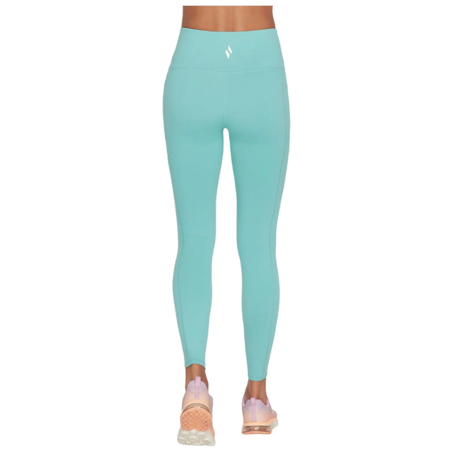 A person is standing in fitted turquoise leggings and light pink sneakers, showcasing a stylish athletic look in a neutral background that highlights the attire.