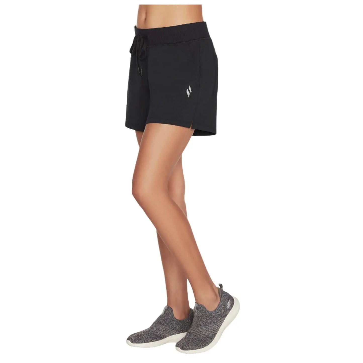 Black shorts with a drawstring waist are being worn by a person standing on one leg in gray sneakers against a plain background. The shorts have a logo on the side.