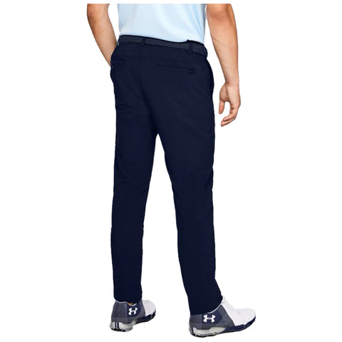 A person is standing with their back facing the viewer wearing navy pants and golf shoes their left hand is relaxed by their side and they are in a neutral outdoor setting