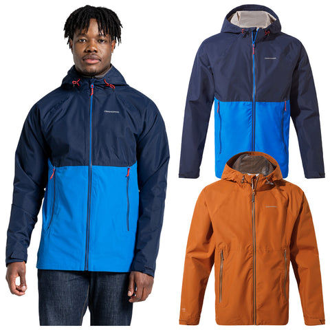 A man is wearing a blue and navy jacket with zippers and a hood he stands confidently while two additional jackets in orange and blue are displayed beside him against a plain background.