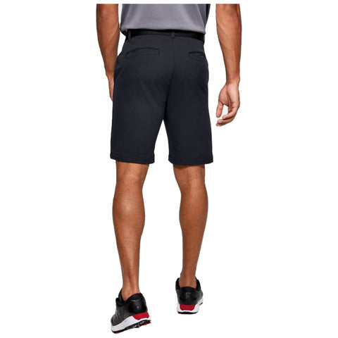 A man is standing with his back to the viewer wearing black shorts and a gray shirt while resting his right hand on his hip in a neutral setting.