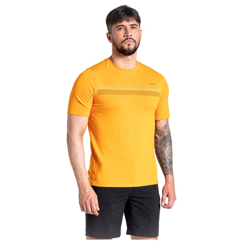 A man stands confidently wearing an orange short-sleeve shirt and black shorts. His tattooed arm is visible, and he looks directly at the viewer against a plain white background.