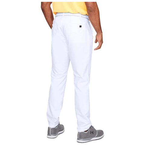 A person stands facing away wearing white golf pants and a yellow shirt with gray shoes in a neutral setting emphasizing the clothing style and athletic appearance.