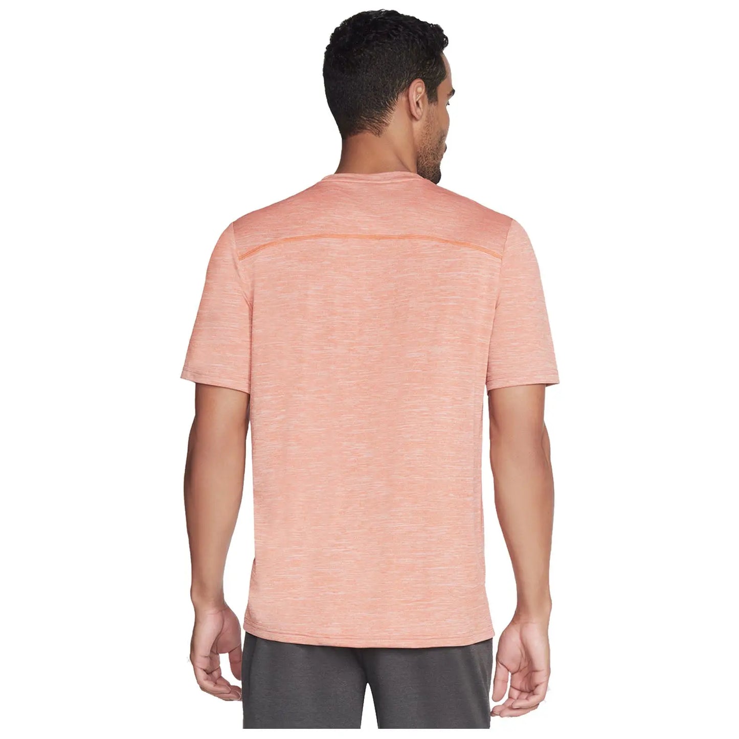 A man is wearing a light orange athletic shirt and gray shorts while standing with his back facing the viewer in a neutral setting without any specific background elements.