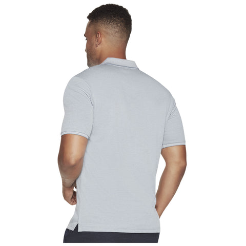 A man stands with his back to the viewer wearing a light gray polo shirt. He has short curly hair and muscular arms, suggesting a casual outdoor setting.