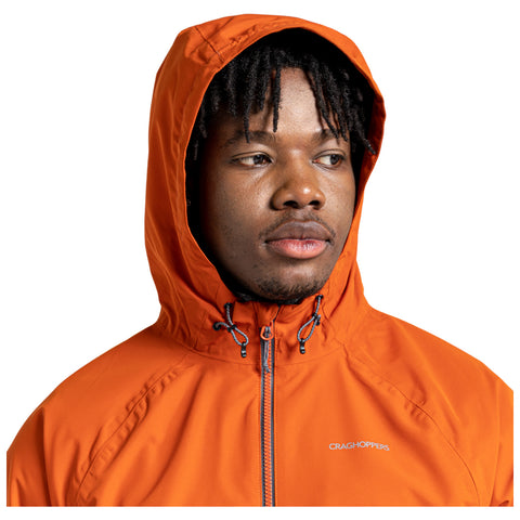 A person wearing an orange hooded jacket looks slightly to the side with a neutral expression against a plain white background. The jacket features a brand logo on the chest.