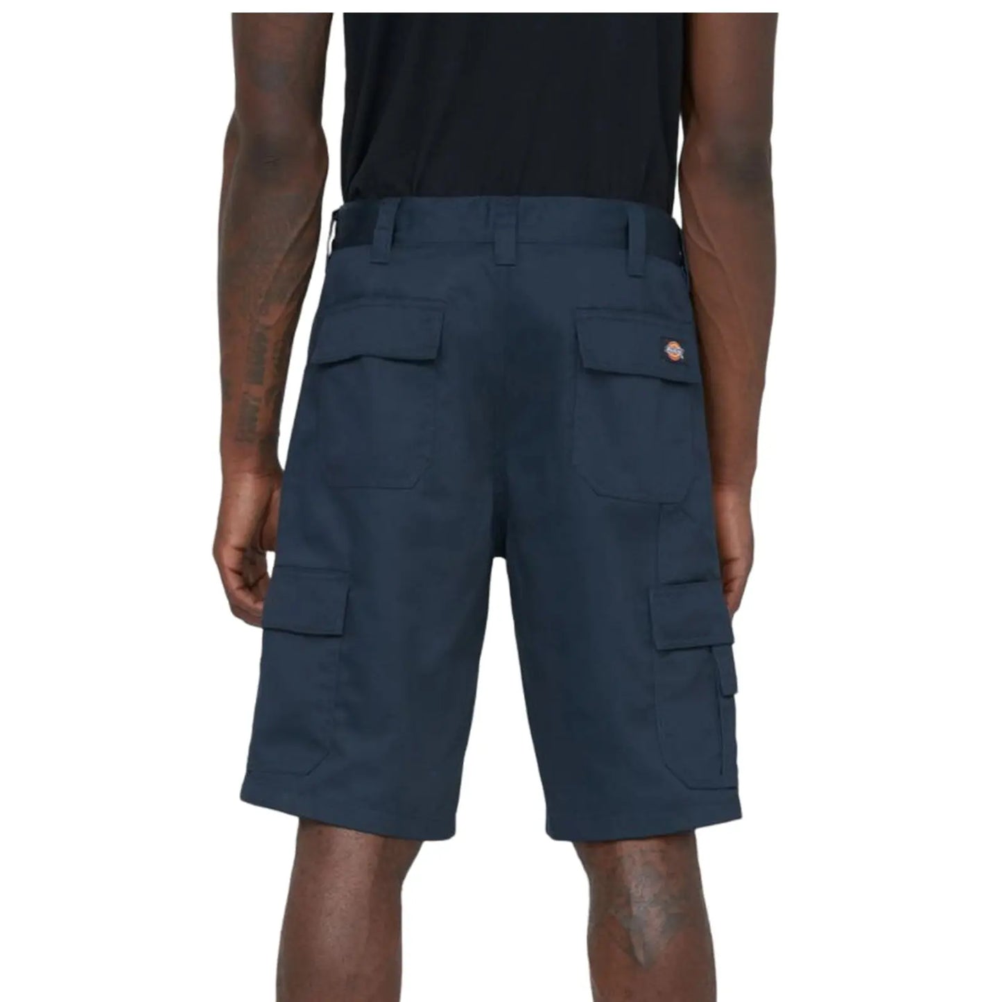Dark cargo shorts are displayed on a person from the back highlighting multiple pockets and a logo on the waistband while standing in an undefined setting.