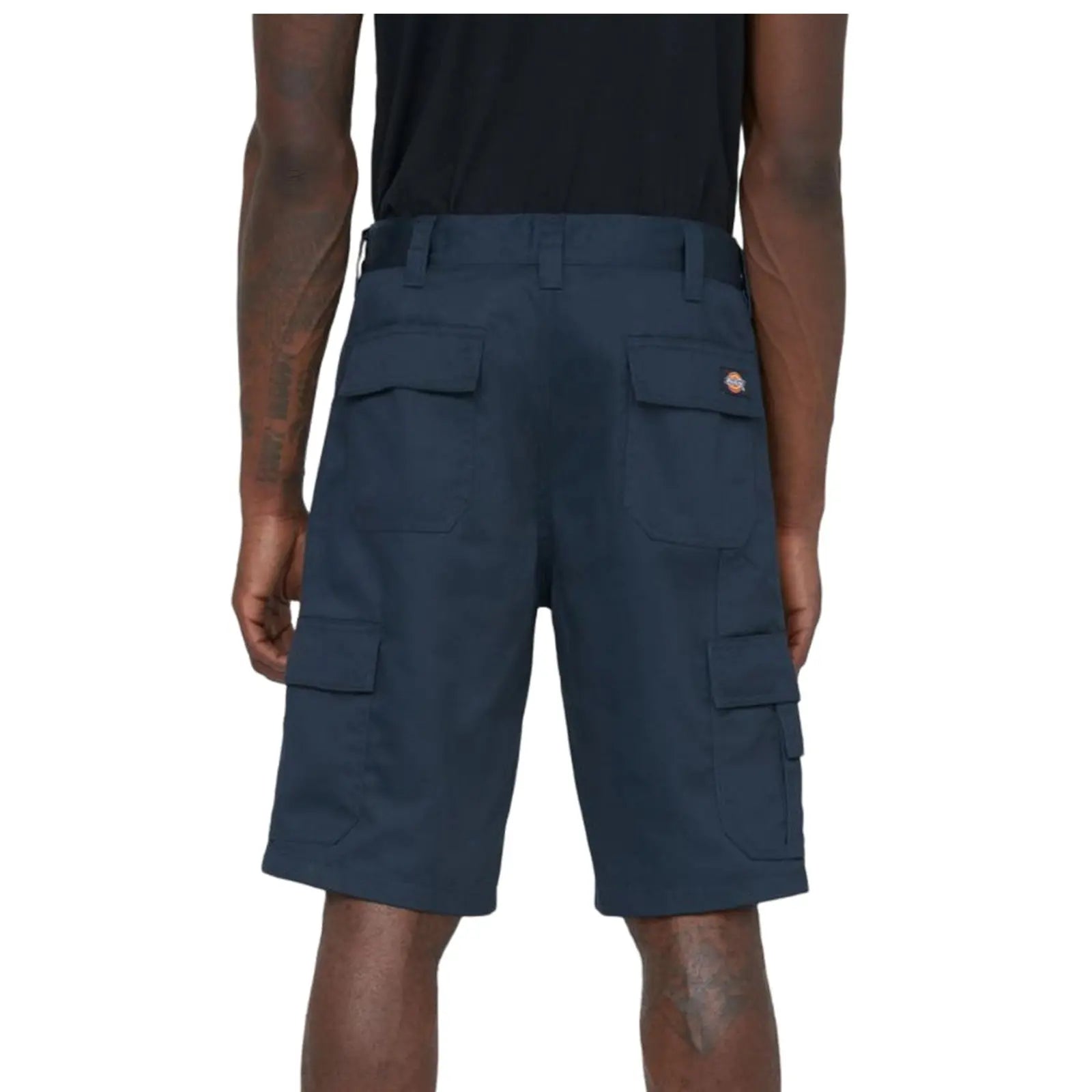 Dark cargo shorts are displayed on a person from the back highlighting multiple pockets and a logo on the waistband while standing in an undefined setting.