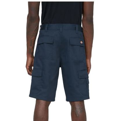 Dark cargo shorts are displayed on a person from the back highlighting multiple pockets and a logo on the waistband while standing in an undefined setting.