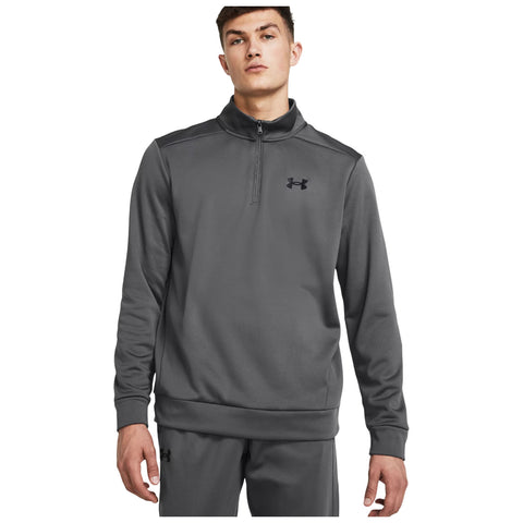 A young man is standing and looking directly at the viewer while wearing a gray zip-up athletic sweatshirt with a black logo on the chest and matching pants.