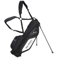 A black and white golf bag equipped with adjustable straps stands upright on its tripod legs with various zippered compartments for storage set against a neutral background.