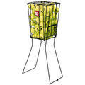 A wire basket filled with yellow tennis balls stands upright on two metal legs in a sports setting, designed for easy access to the balls during practice or training.