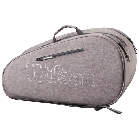 A gray tennis bag with a prominent white Wilson logo is resting on a flat surface featuring multiple compartments and a top handle for carrying.
