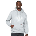 A young man is smiling while wearing a gray hoodie with a logo on the front. He has one hand in the pocket and is standing against a plain background.