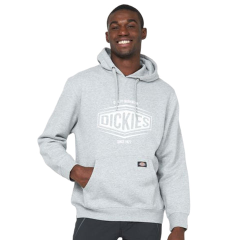 A young man is smiling while wearing a gray hoodie with a logo on the front. He has one hand in the pocket and is standing against a plain background.