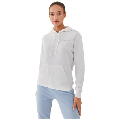 A woman poses wearing a white hoodie with a front pocket and light blue pants showcasing a relaxed casual style in a bright setting.