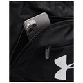 A black backpack features a partially unzipped pocket containing a smartphone with a three-camera arrangement visible on its back while the backpack's logo is also prominently displayed.