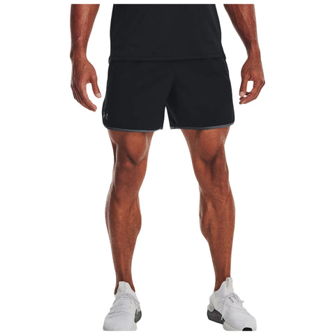 A male figure stands upright wearing black athletic shorts and white shoes showcasing muscular legs while a dark shirt partially visible above emphasizes an active appearance in a neutral background.