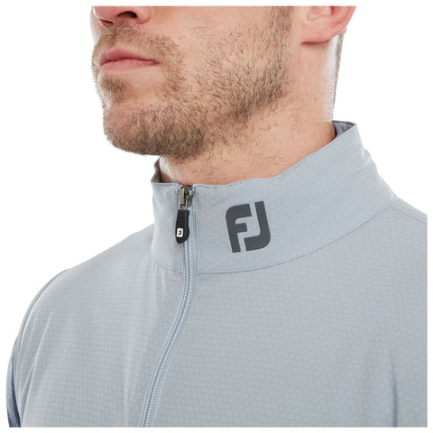 A man is wearing a light gray zipped jacket with a high collar displaying the logo FJ on the left side. His facial expression is neutral and focused.