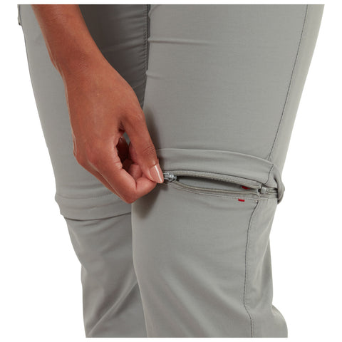 A hand is pulling a zipper on the knee area of light gray pants showcasing adjustable length functionality in a neutral setting with no additional background detail.