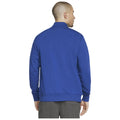 A man is wearing a bright blue sweatshirt and gray pants facing away from the viewer in a simple, well-lit environment