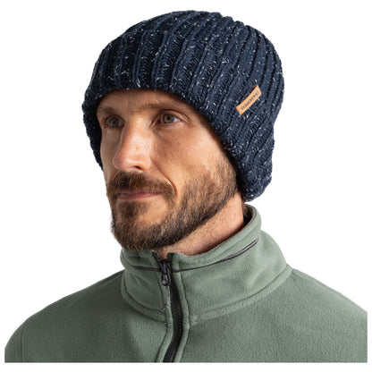 A man wears a dark ribbed knit beanie and a green fleece jacket while looking thoughtfully to the side against a plain white background.