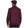 A man stands with his back facing the viewer wearing a dark burgundy pullover with a collar in a plain background emphasizing the clothing.