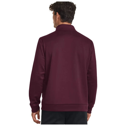 A man stands with his back facing the viewer wearing a dark burgundy pullover with a collar in a plain background emphasizing the clothing.